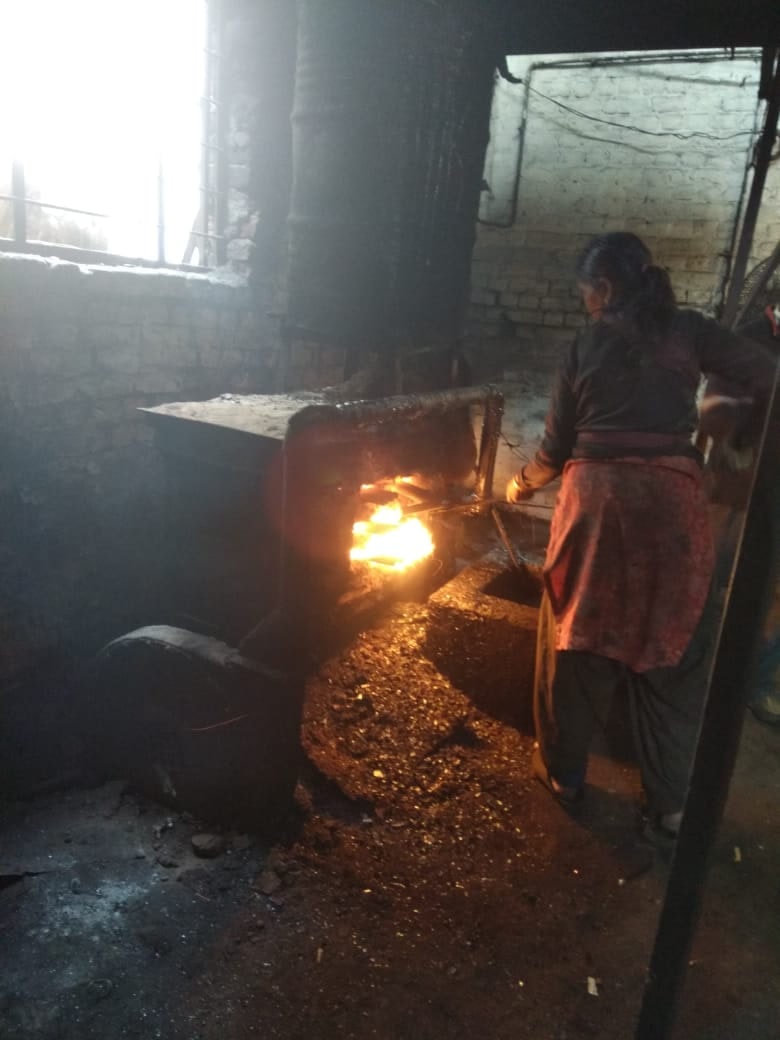 The interior of a small brick-walled furnace works, an open fire burning in the mouth of the kiln while a worker feeds it from the side.