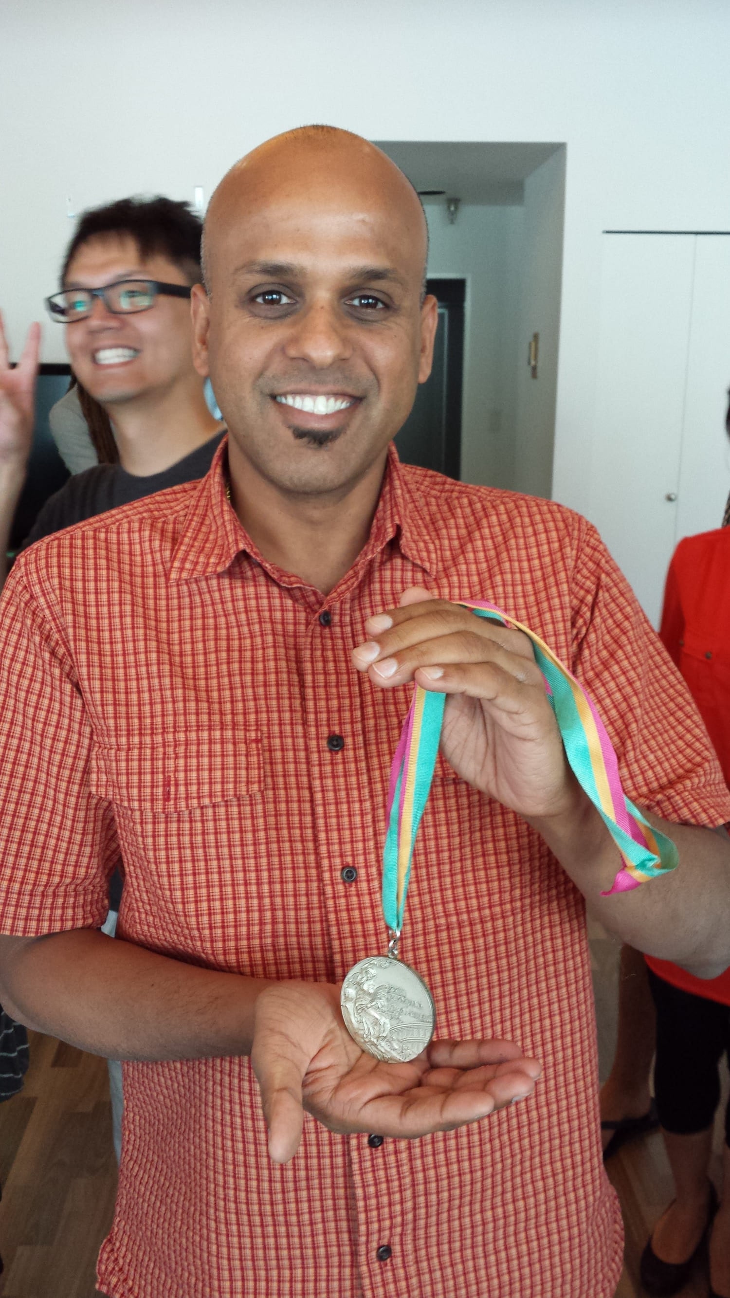 Manuj Aggarwal holding a silver medal on a ribbon, smiling, with colleagues behind him.